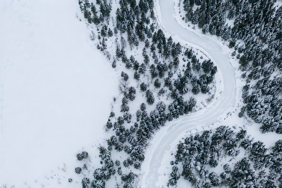 Aerial view of a snow-covered forest with a winding frozen river and a wide open snowfield for copy space