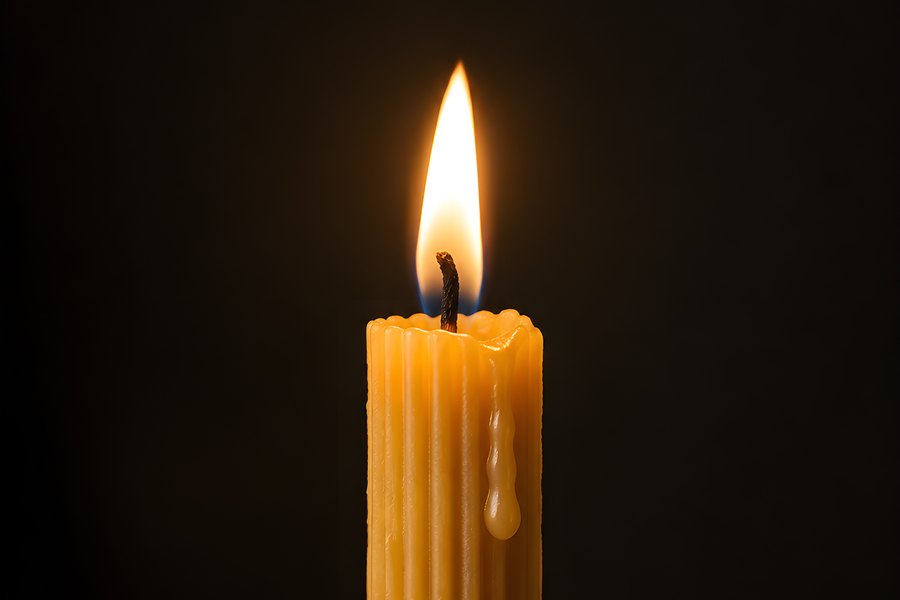 Single ribbed pillar candle burning in a brass holder with dripping wax against a black background