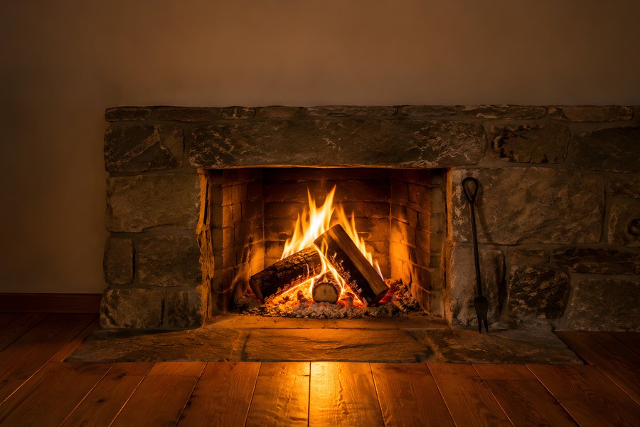Cosy stone fireplace with burning logs and glowing embers on a rustic wood floor, warm evening interior with no people