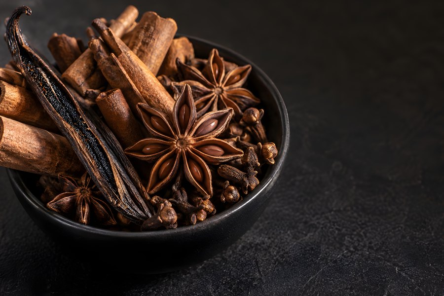 Warm autumn baking spices in a dark bowl with cinnamon sticks, star anise, cloves and a split vanilla pod on a moody textured surface