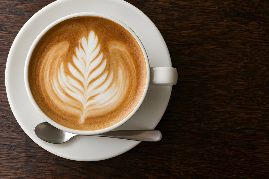 Rosetta latte art in a white cappuccino cup on a dark wood table, overhead flat lay with copy space