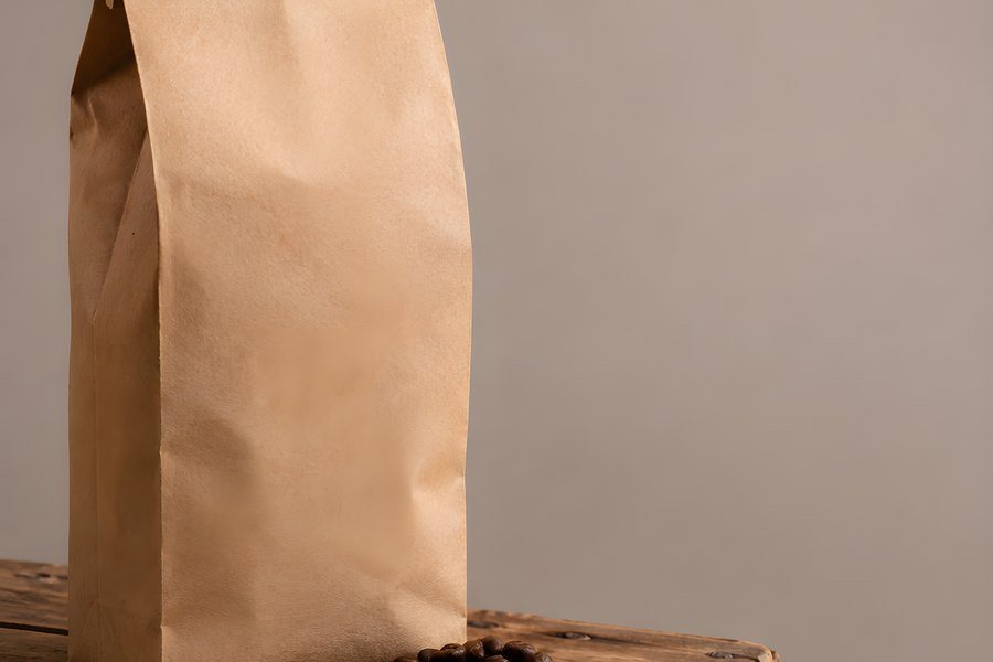 Blank kraft paper coffee bag with tin-tie closure and spilled roasted coffee beans on a weathered wooden crate