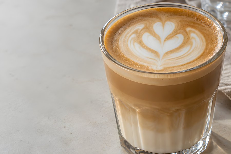 Tulip latte art in a faceted glass with layered milk coffee, golden crema, and soft natural light on a marble tabletop with copy space