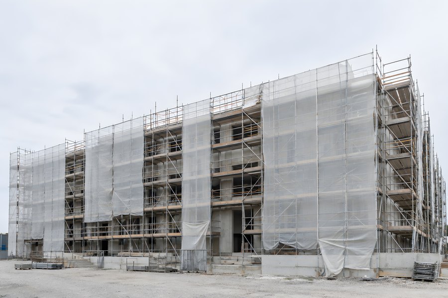 Multi-story building facade wrapped in steel tube scaffolding and protective mesh forming a repeating geometric pattern, no people