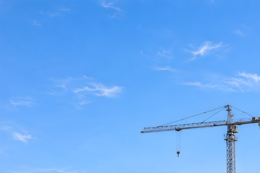 Tower crane jib and lattice mast silhouetted against a clear blue sky with wispy clouds and copy space