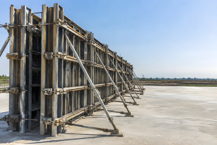 Row of steel formwork panels braced with diagonal props beside a concrete slab construction site