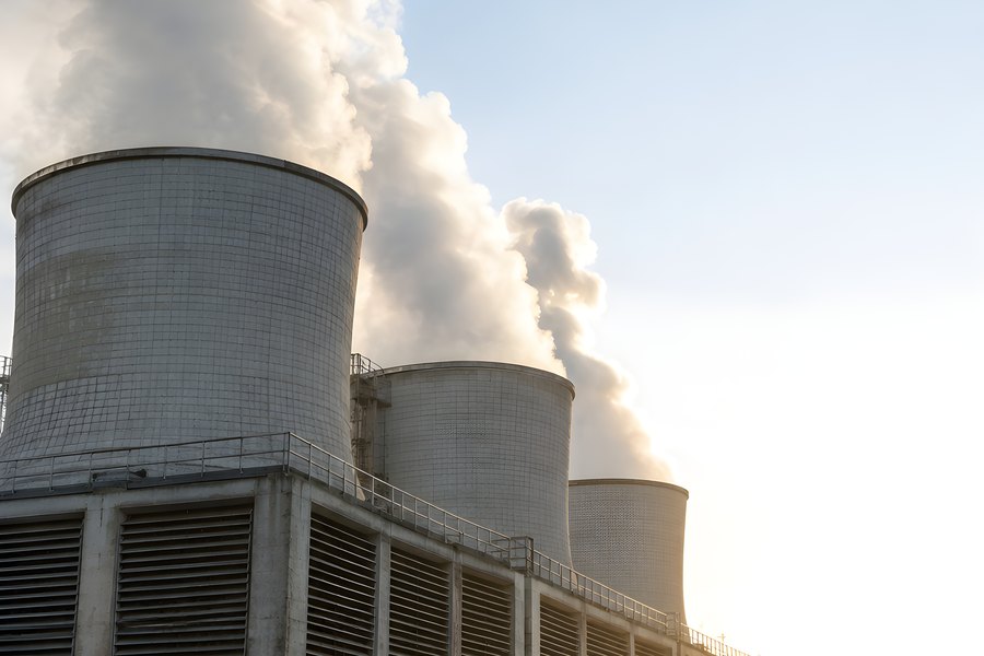 Industrial cooling towers releasing tall steam plumes at sunrise above a still water reservoir