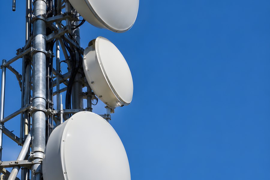 Microwave relay dishes mounted on a lattice telecom tower against a clear blue sky