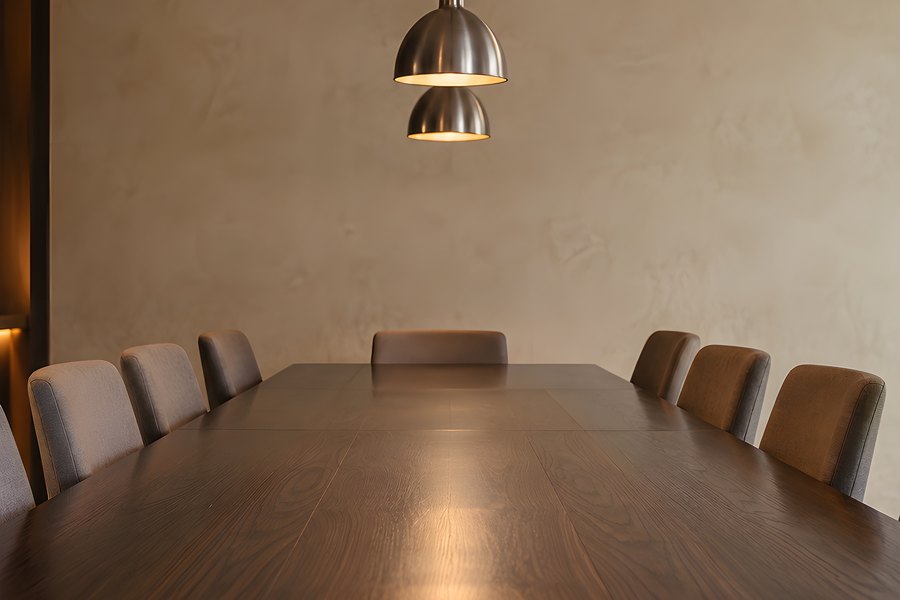 Empty Formal Boardroom with Long Wood Table, Upholstered Chairs and Tiered Pendant Lights Against a Warm Textured Wall
