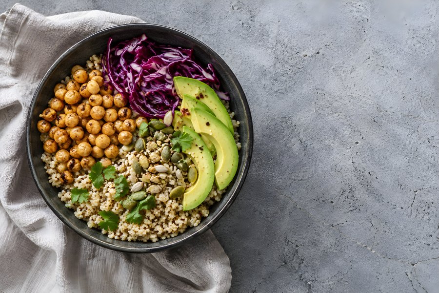 Overhead view of a vegetarian quinoa buddha bowl with roasted chickpeas, red cabbage and avocado on a grey concrete background with copy space