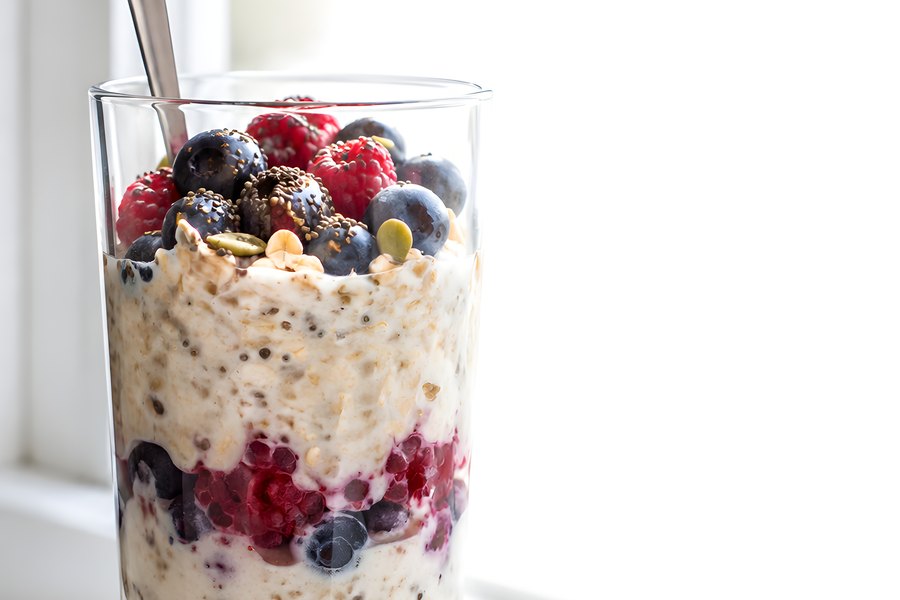 Layered Overnight Oats Jar with Fresh Berries, Chia Seeds and a Spoon on a Sunlit Windowsill