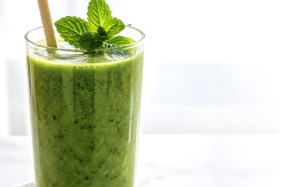 Fresh green smoothie in a clear glass topped with mint leaves and a paper straw, served on a linen napkin over a marble surface