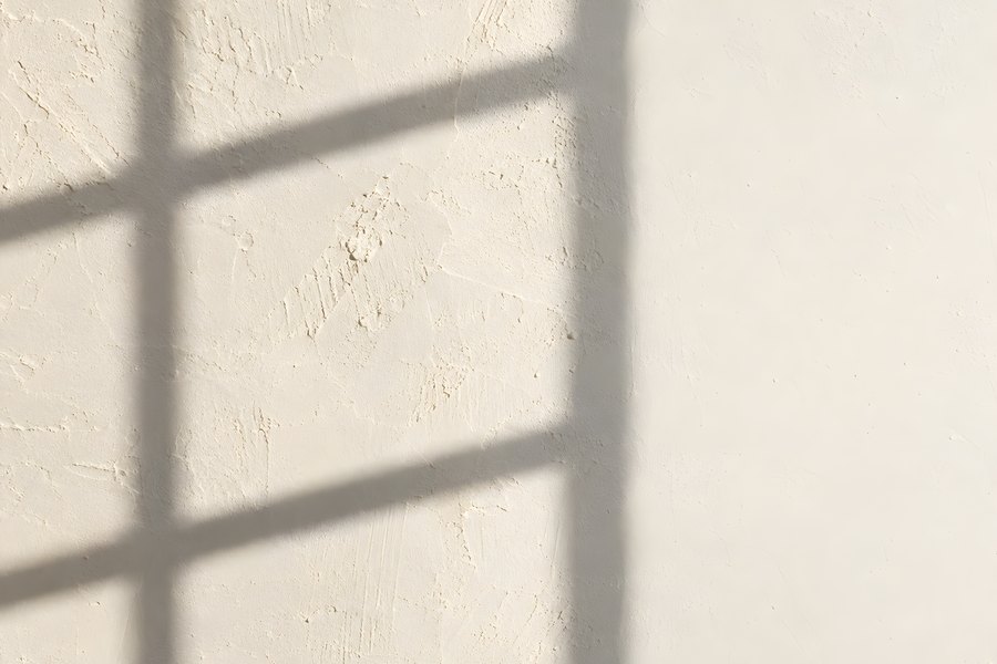 Window Grid Shadow Falling Across a Textured Plaster Wall in an Empty Sunlit Interior