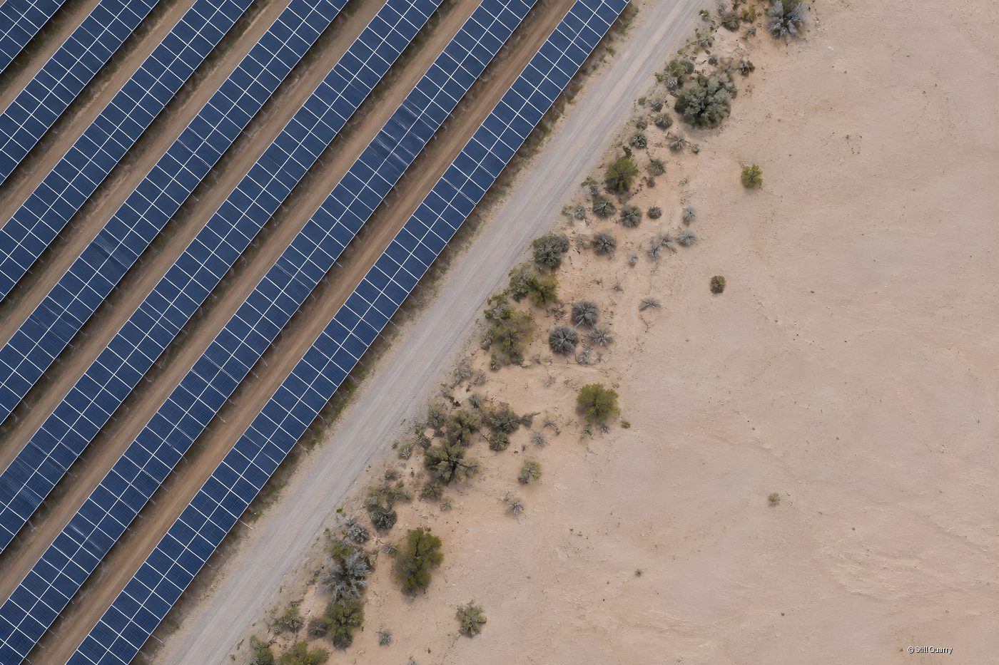 Aerial top-down view of a utility scale solar farm with photovoltaic panel rows beside a gravel road and arid desert land