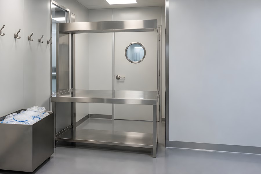 Empty cleanroom gowning room with stainless steel bench, wall hooks and a round window airlock door in a sterile pharmaceutical facility