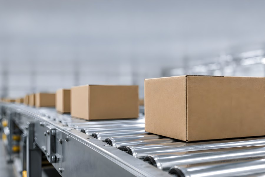 Close-up of cardboard boxes on a metal roller conveyor inside a warehouse distribution centre, no people visible