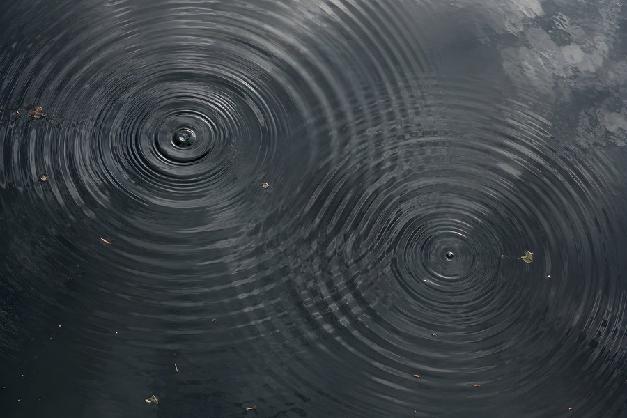 Concentric Water Ripples Spreading Across a Calm Dark Pond with Soft Cloud Reflections, Aerial View