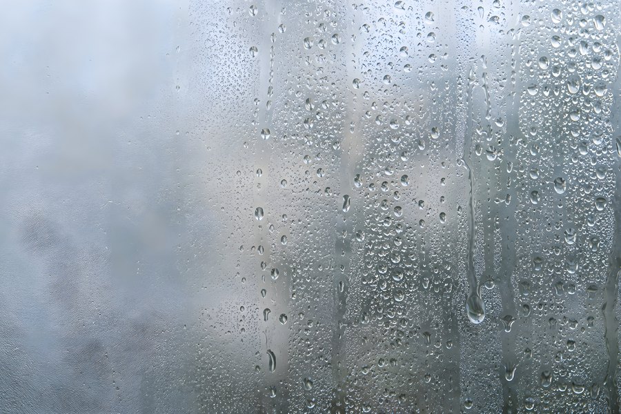 Condensation droplets and rivulets running down a misted glass window pane with blurred background