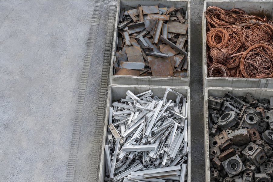 Sorted scrap metal bins at a recycling yard with steel, copper wire, aluminium profiles and cast metal parts seen from above