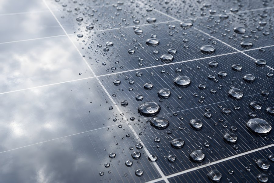 Close-up of raindrops on a dark solar panel with cloudy sky reflected in the glass, photovoltaic cell texture background
