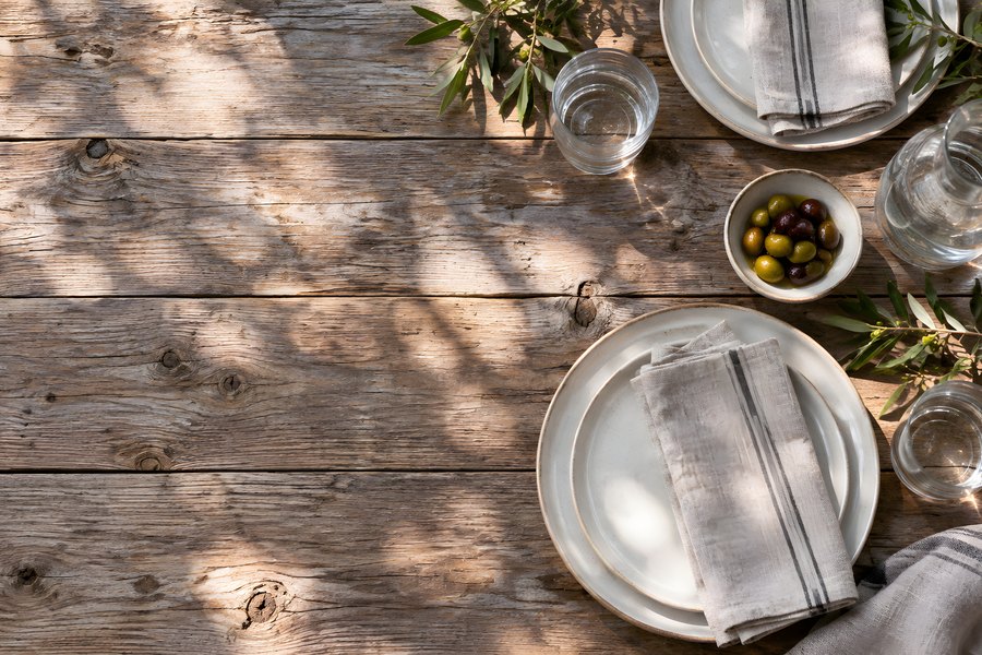Empty Outdoor Dining Table Set for Two on Rustic Wood Terrace with Olives and Dappled Sunlight