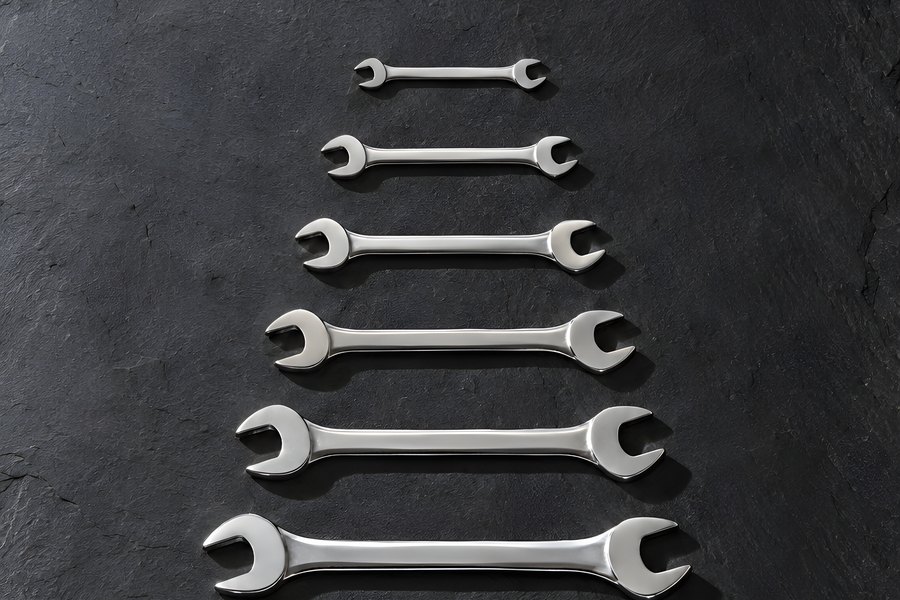 Chrome open-end wrenches in graduated sizes with a bolt, flat lay on a dark slate surface with copy space