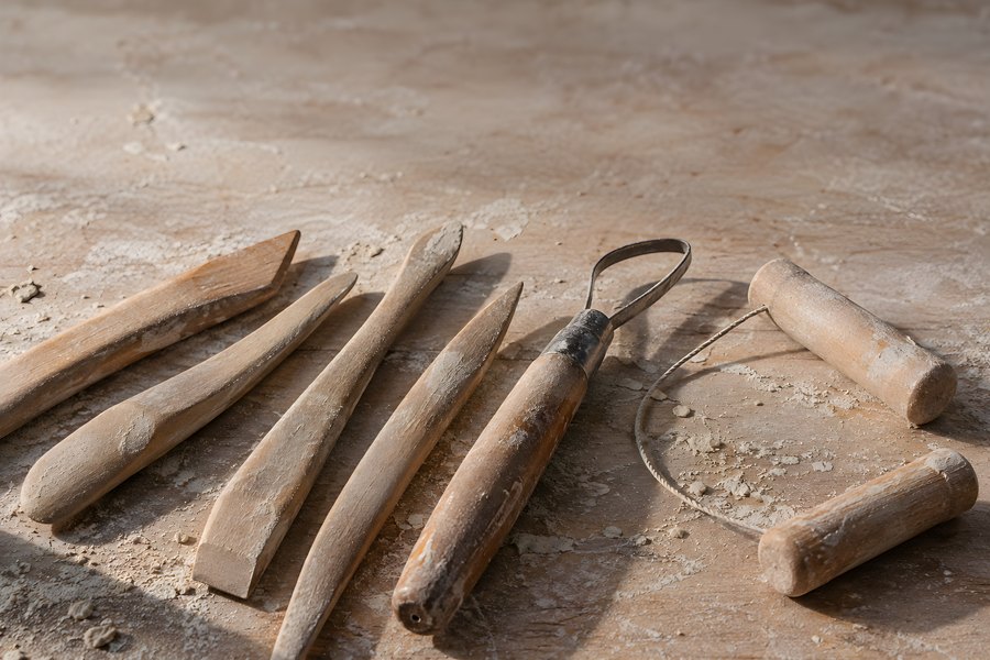 Wooden clay modelling tools and wire cutter arranged on a dusty ceramic studio workbench, no people