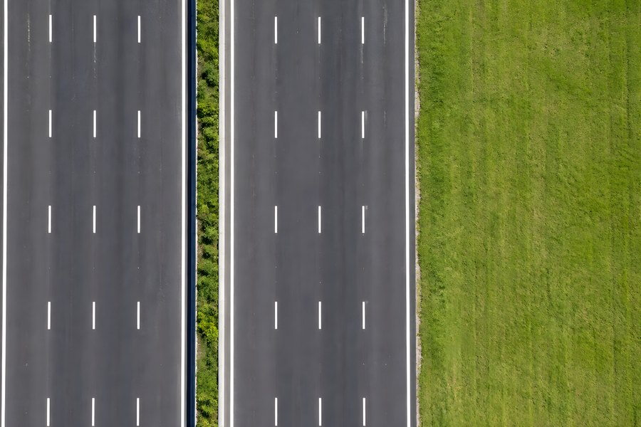 Aerial top-down view of an empty divided highway with dashed lane markings and a grassy median, no traffic