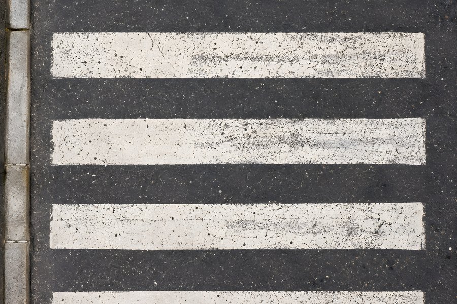 Top-down view of a weathered zebra crossing with cracked white paint on dark asphalt beside a stone curb, no vehicles or people