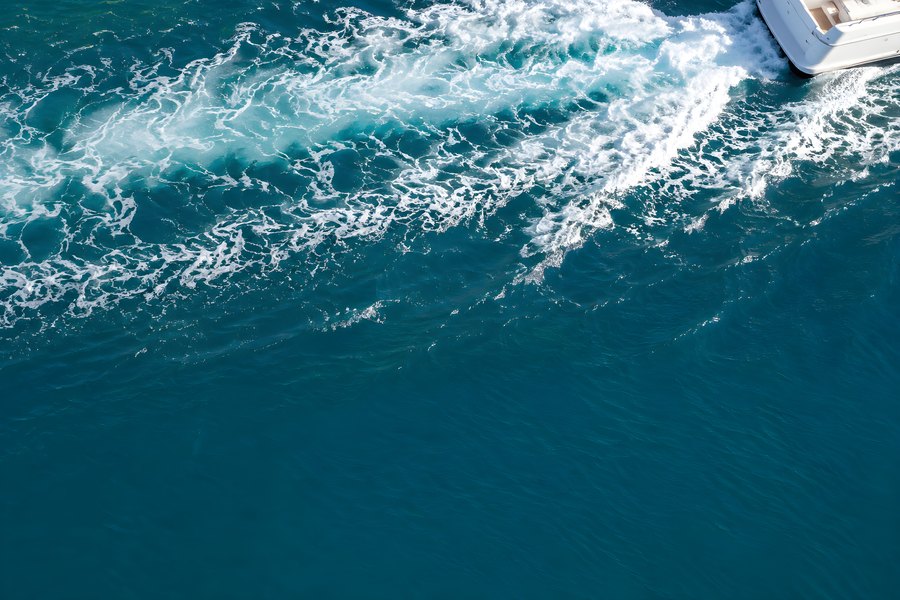 Aerial top-down view of a motorboat's white foam wake trailing across deep turquoise ocean water