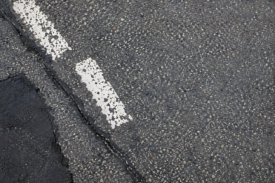 Aerial top-down view of a worn white dashed road line on cracked, textured asphalt