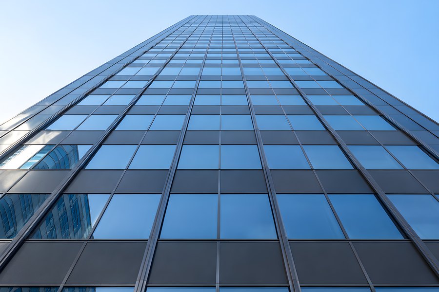 Low-Angle View of a Glass Curtain Wall Skyscraper Against a Clear Blue Sky