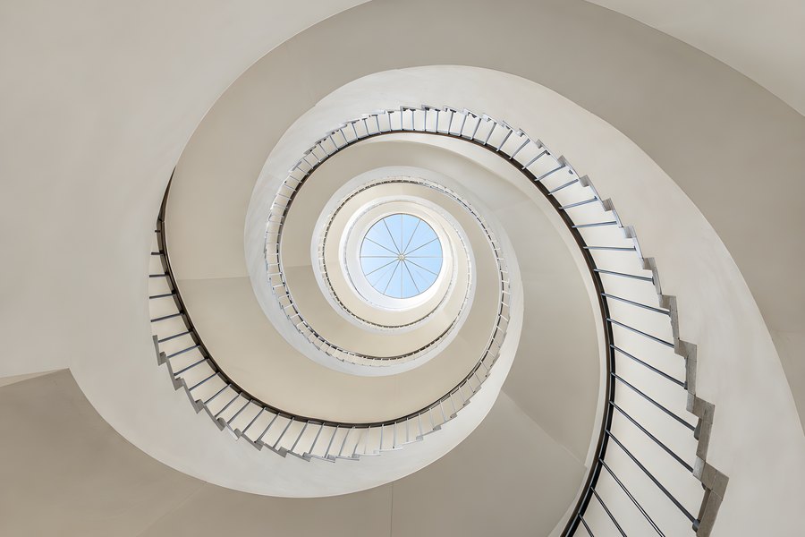 Spiral staircase from above with concrete steps, dark metal handrail and a circular skylight at the center, no people