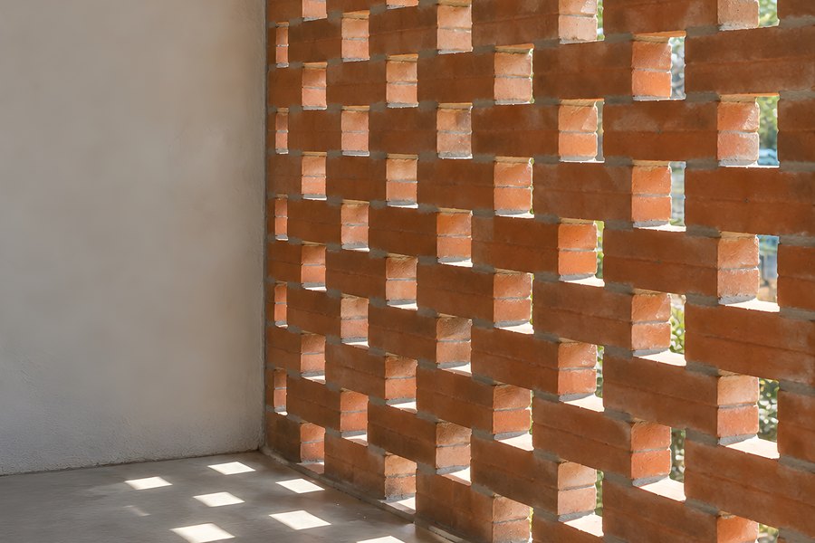 Perforated red brick screen wall in woven bond pattern casting geometric shadows on polished concrete floor