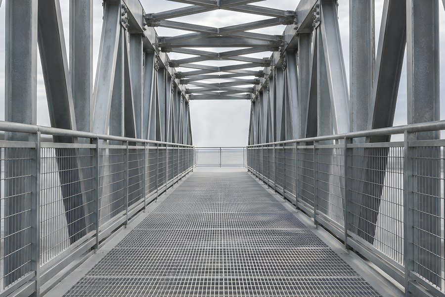 Steel Truss Pedestrian Bridge Walkway with Metal Grating Deck and Mesh Railings Under Overcast Sky
