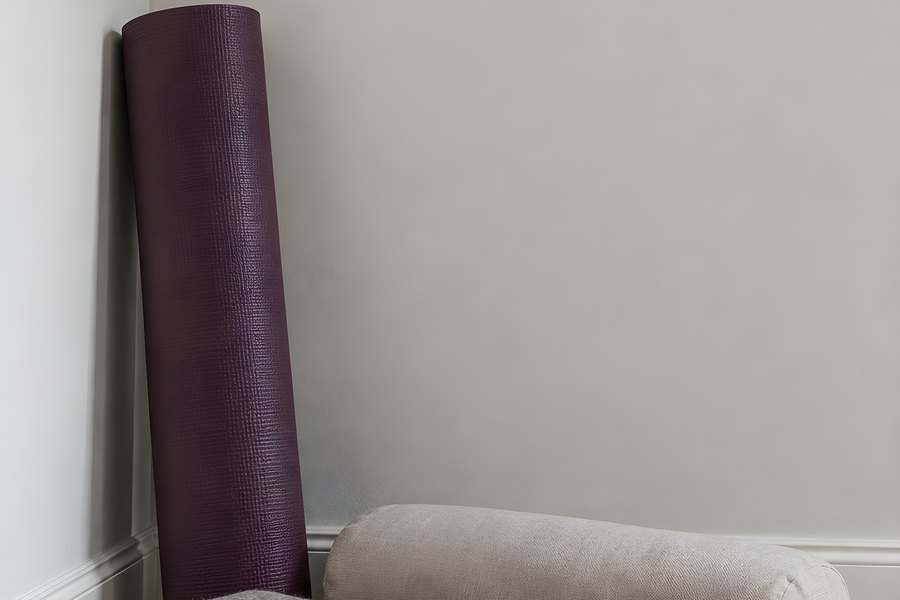 Rolled purple yoga mat, folded blanket and bolster cushion arranged in a minimalist room corner with copy space
