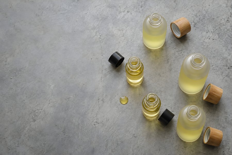 Unlabelled frosted glass oil bottles with wooden and black caps on a grey stone surface with copy space