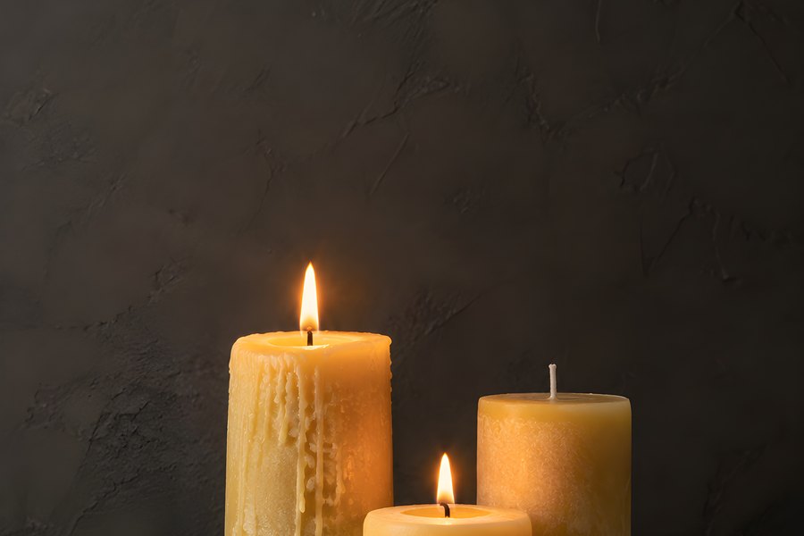 Three beeswax pillar candles of varying heights burning on a round stone tray against a dark textured wall with copy space